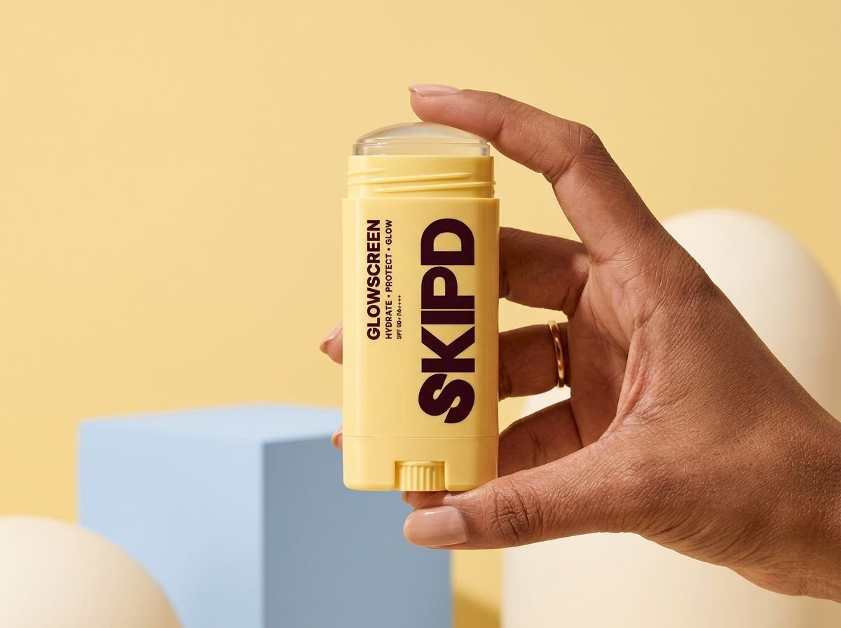 A hand holding Glowscreen on a butter-yellow background